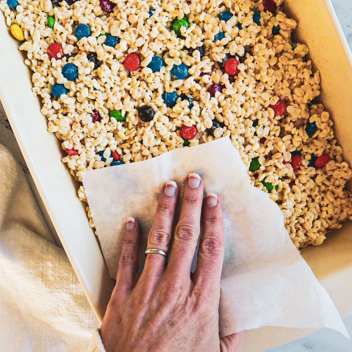 White hand pressing down on pan of bars with parchment paper.