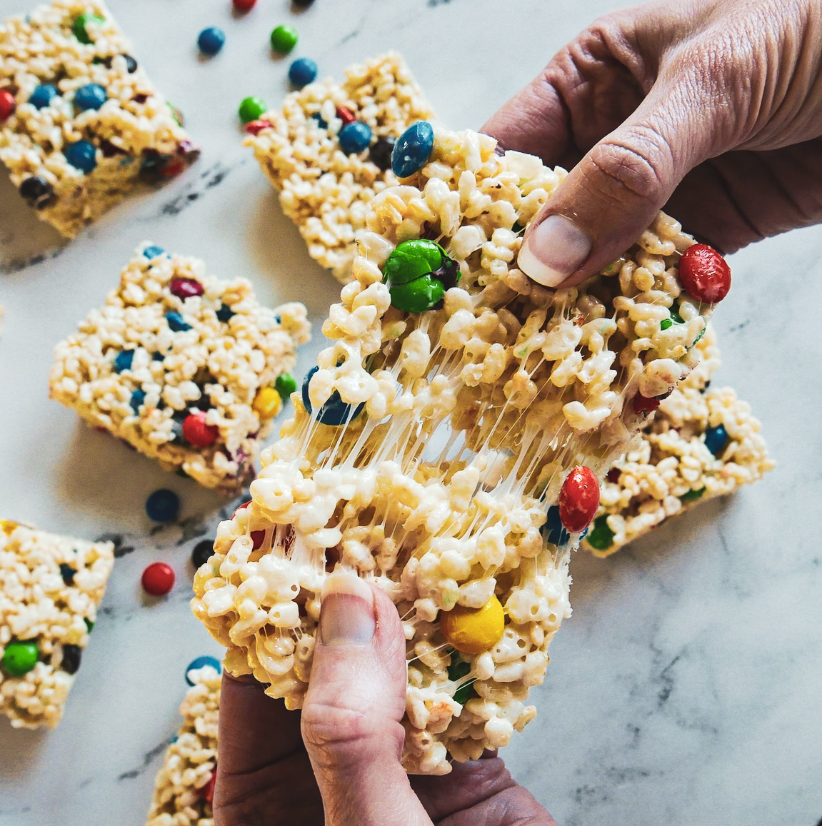 Hand pulling apart rice krispie treats with more on the table.