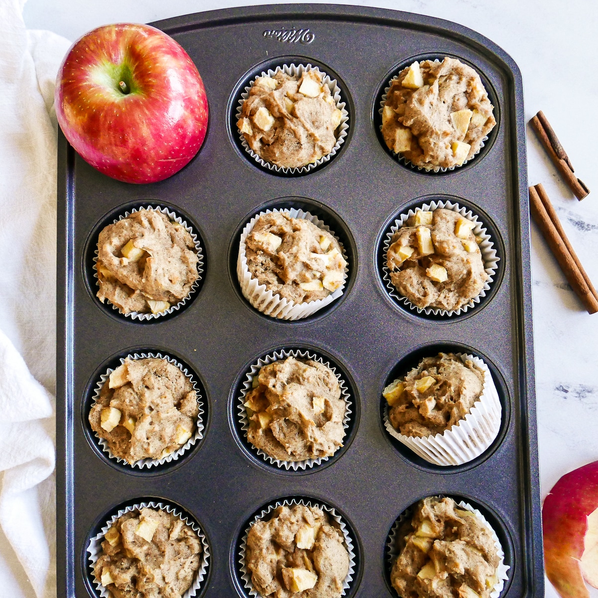 baked apple muffins in tin with cinnamon sticks and apple.