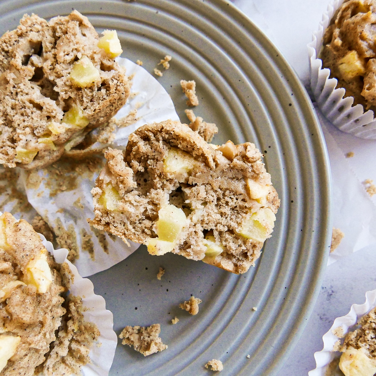Sliced apple muffins on a gray plate with crumbs.