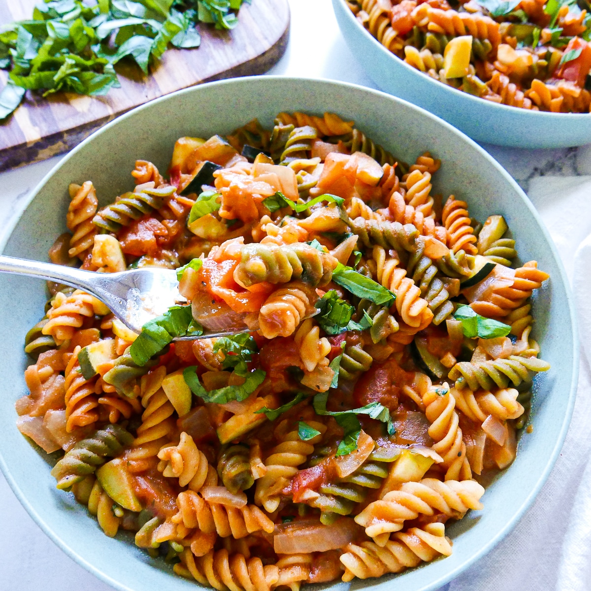 fork lifting up bite of pasta with sauce with another bowl in background. 