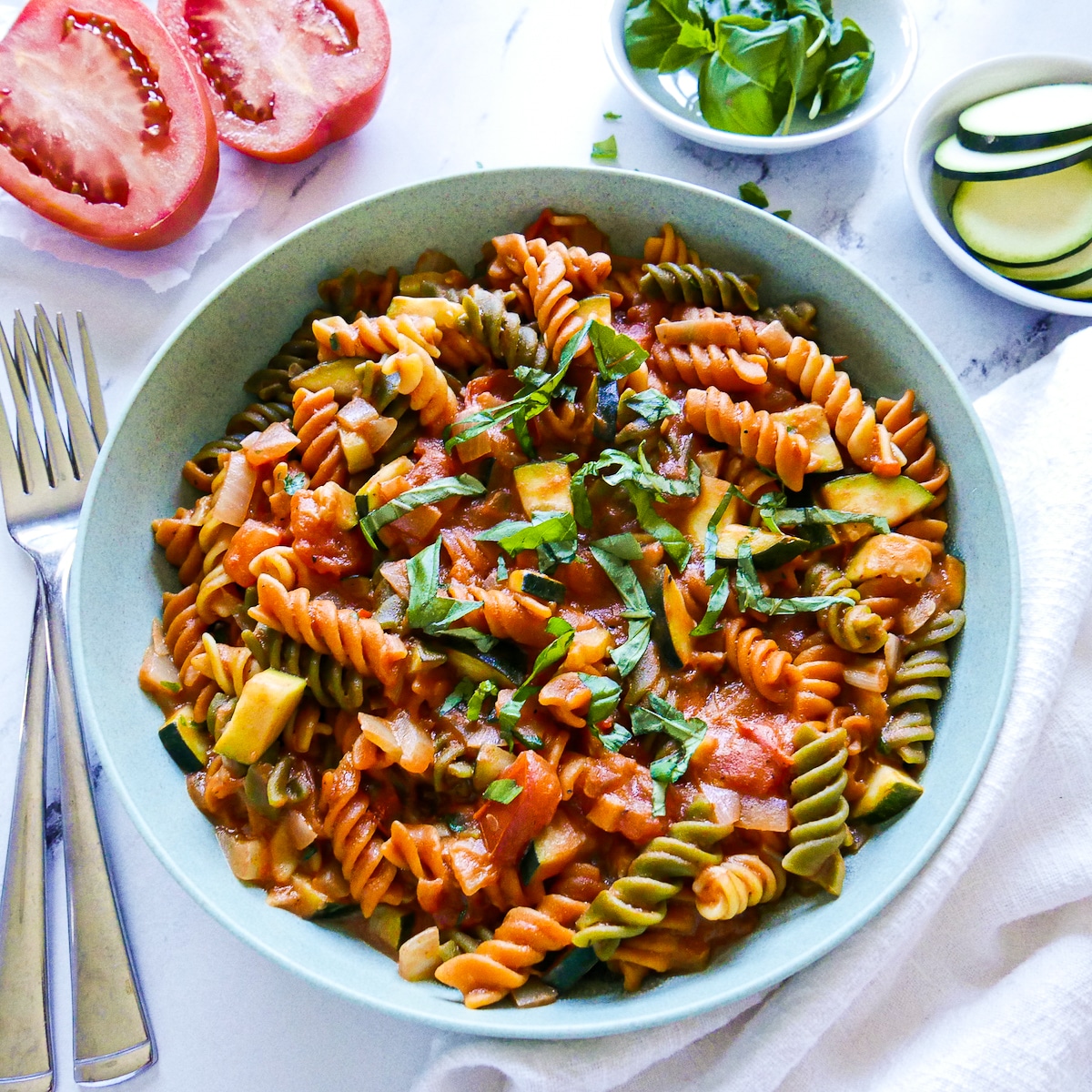 large bowl of vegetarian pasta garnished with fresh basil with two forks on the side.