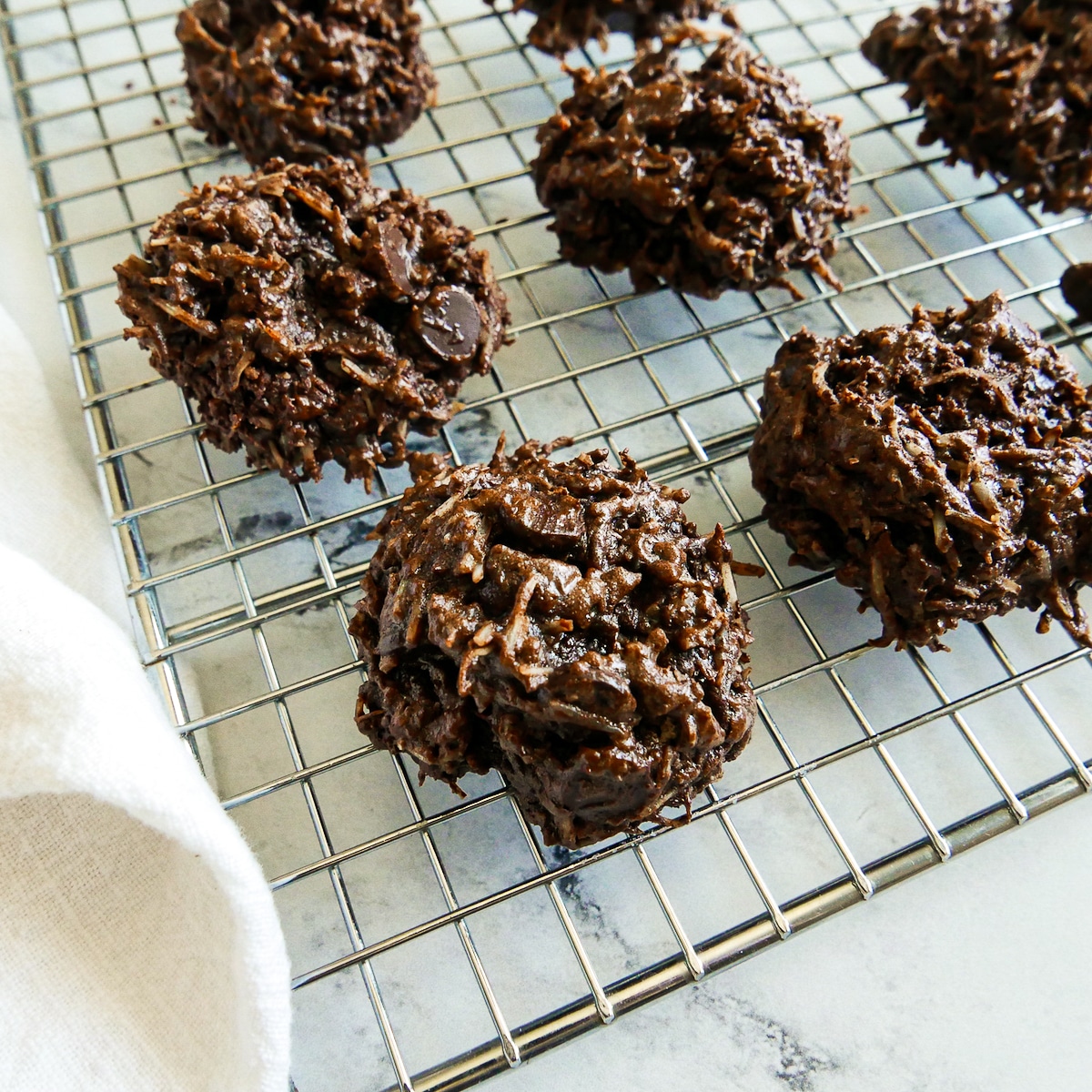 Baked macaroons placed on a cooling rack with a white napkin next to it. 