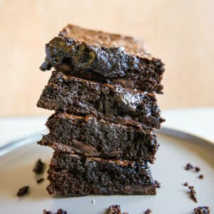 Four dairy free chocolate brownies stacked on a gray plate.
