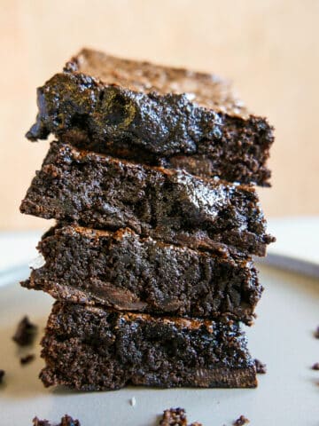 Four dairy free chocolate brownies stacked on a gray plate.