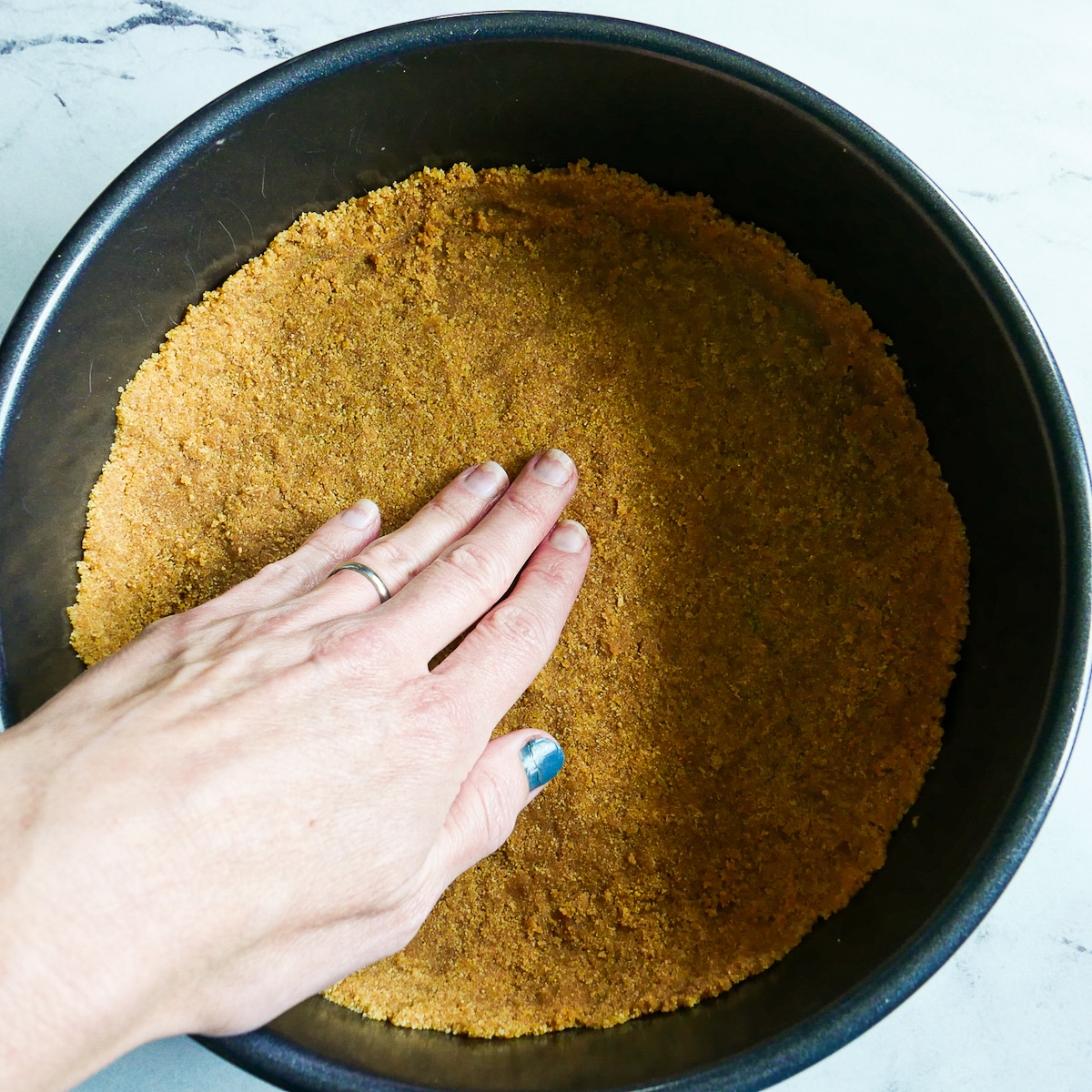 Hand pressing graham cracker crust into springform pan.