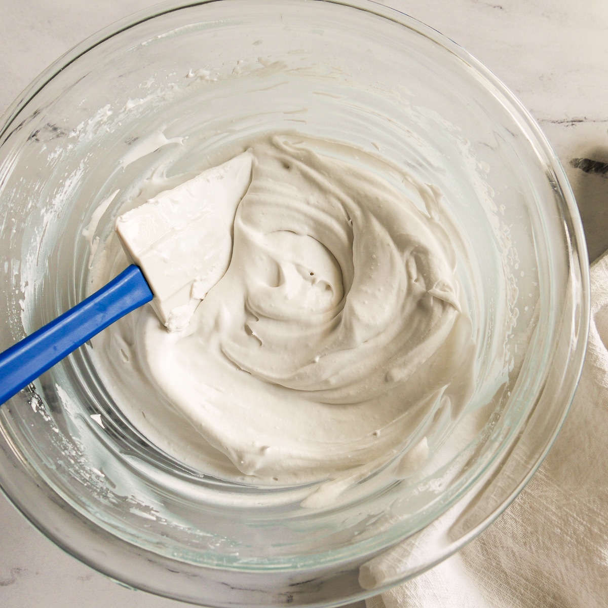 coconut whipped cream in a glass bowl with a spatula.