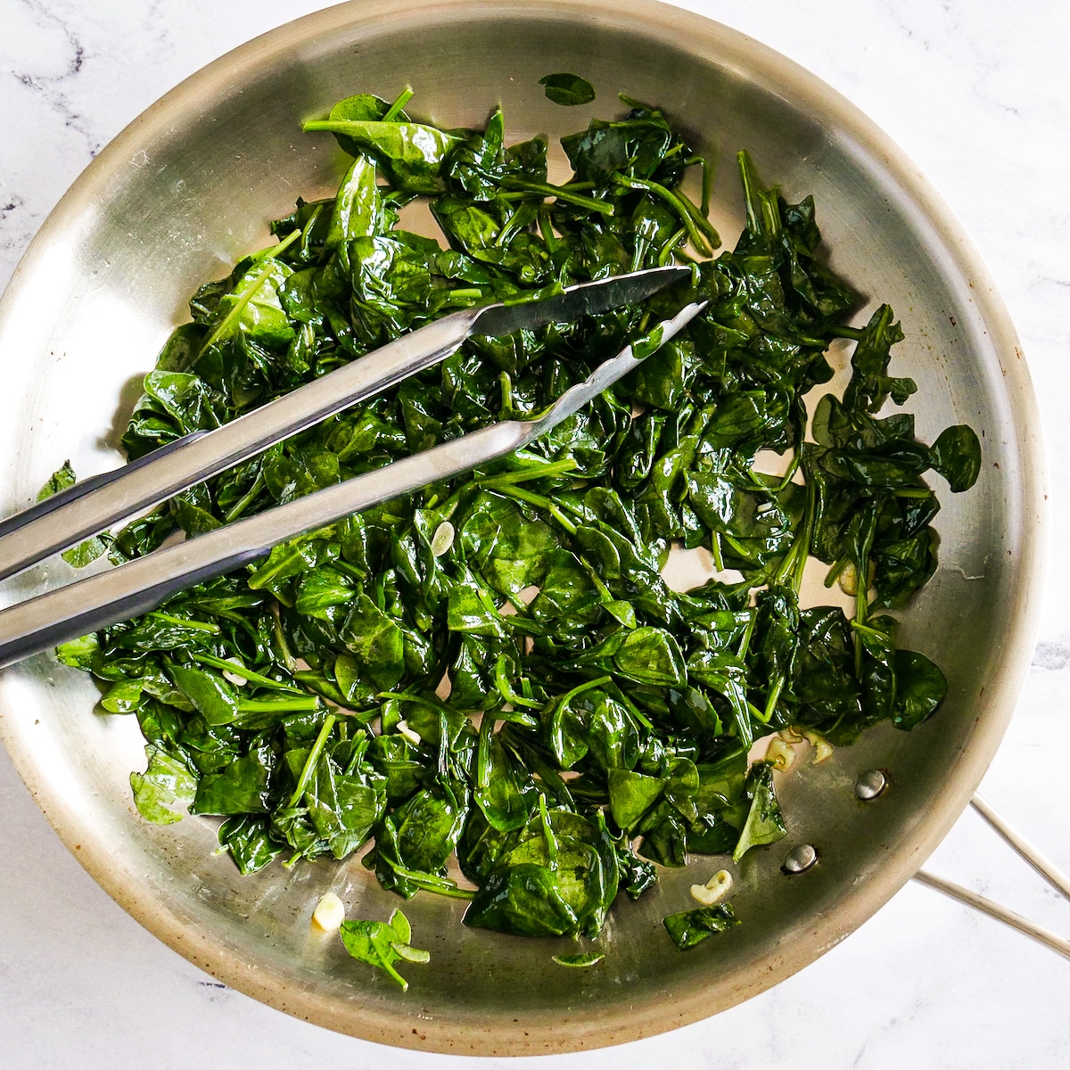 Wilted spinach and garlic sauteed in a large skillet.