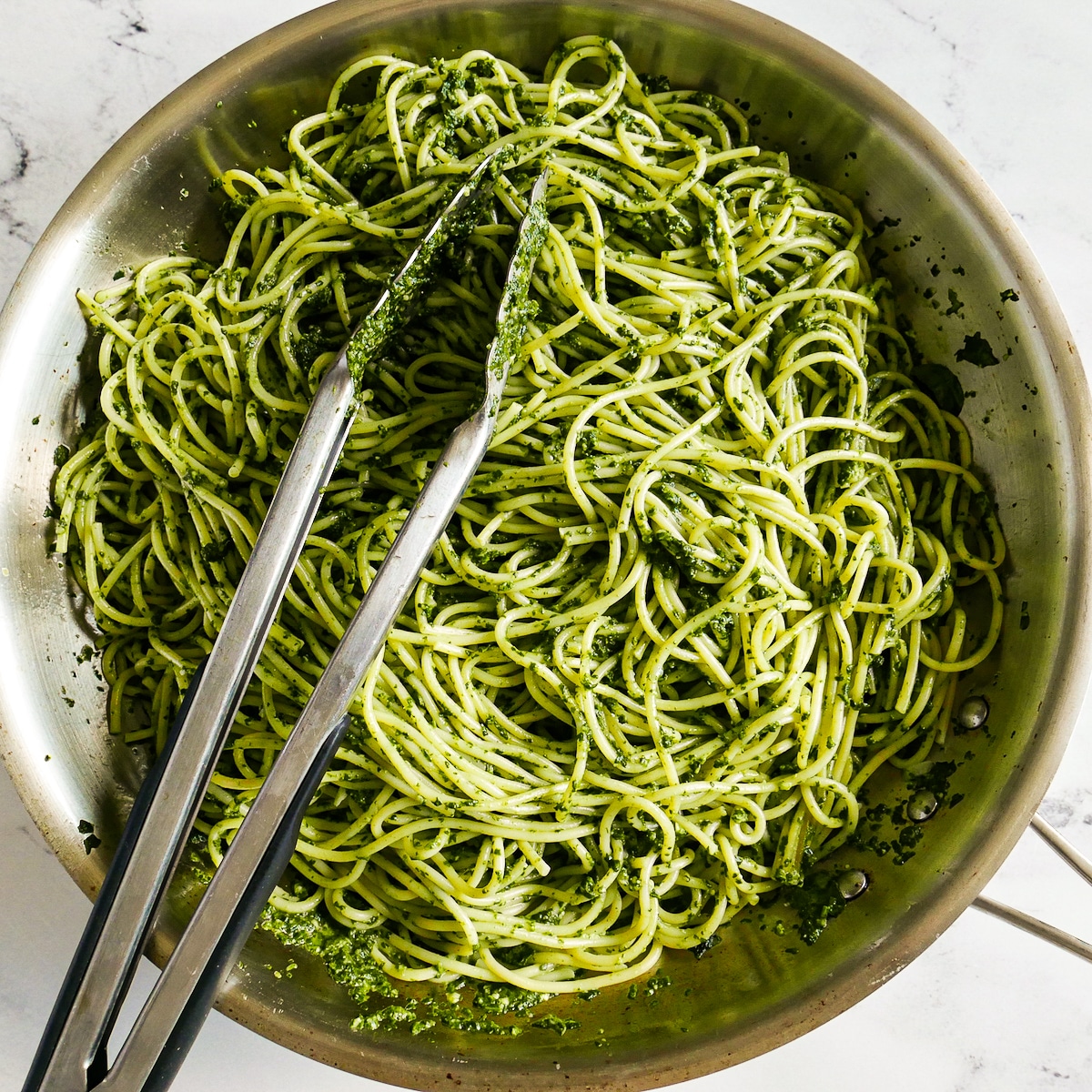 Noodles tossed with sauce in a skillet with tongs.