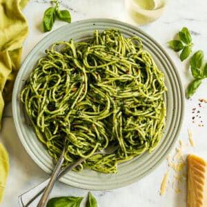 Spaghetti with green pasta sauce on a large platter garnished with fresh basil.