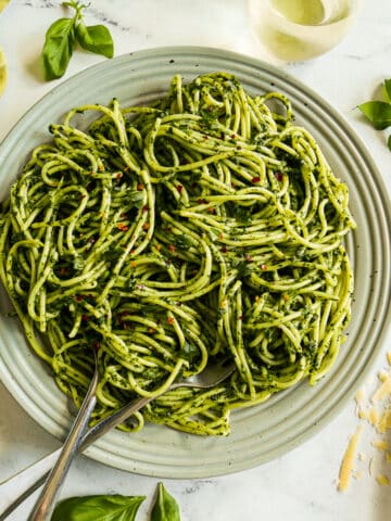 Spaghetti with green pasta sauce on a large platter garnished with fresh basil.