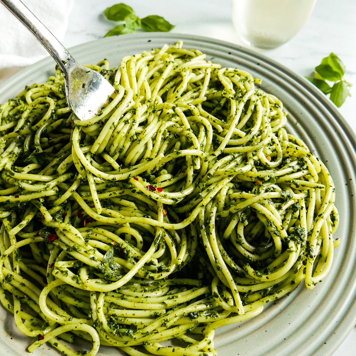 Fork twirling noodles on a gray plate with wine in the background.