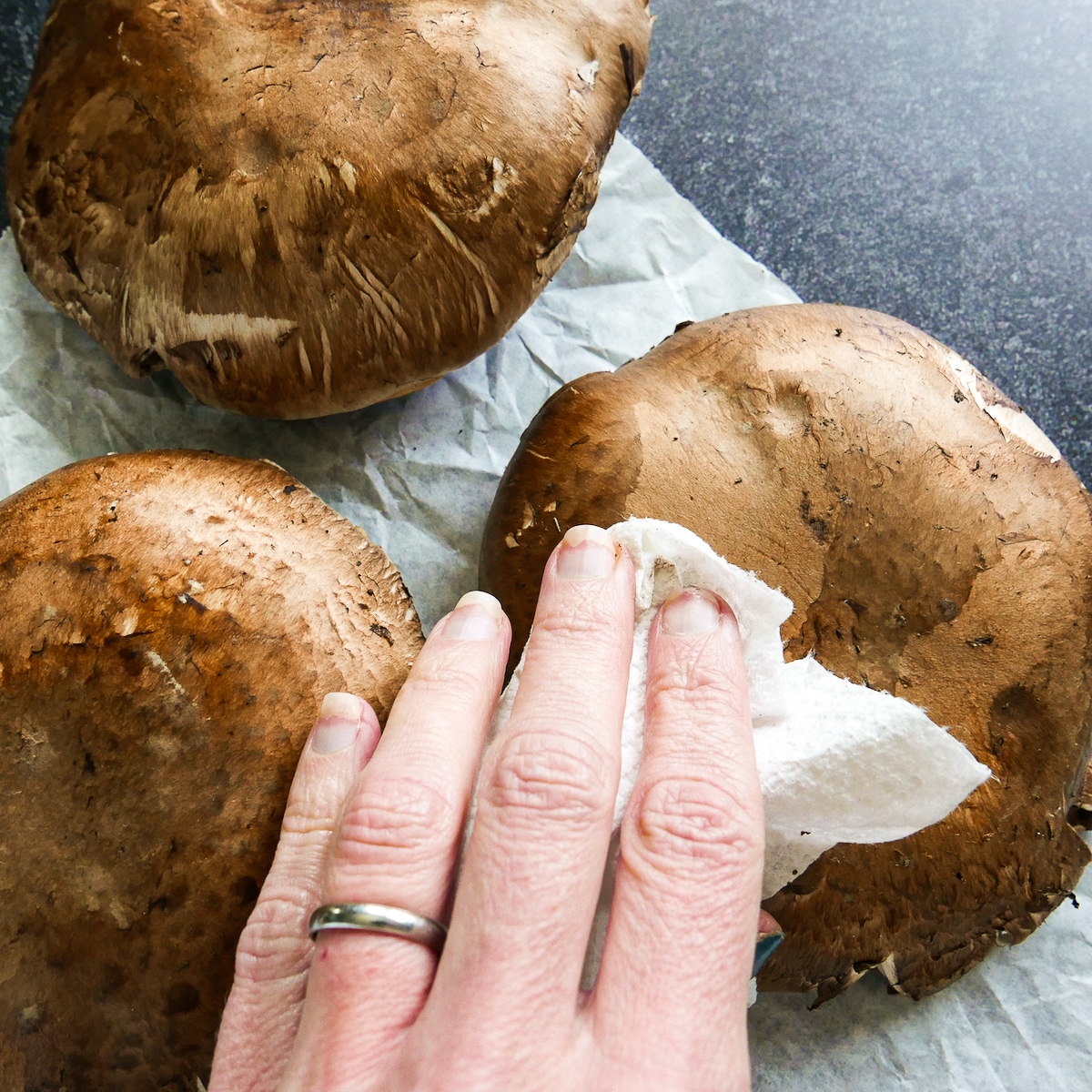 Hand wiping portobello mushrooms clean with a paper towel.
