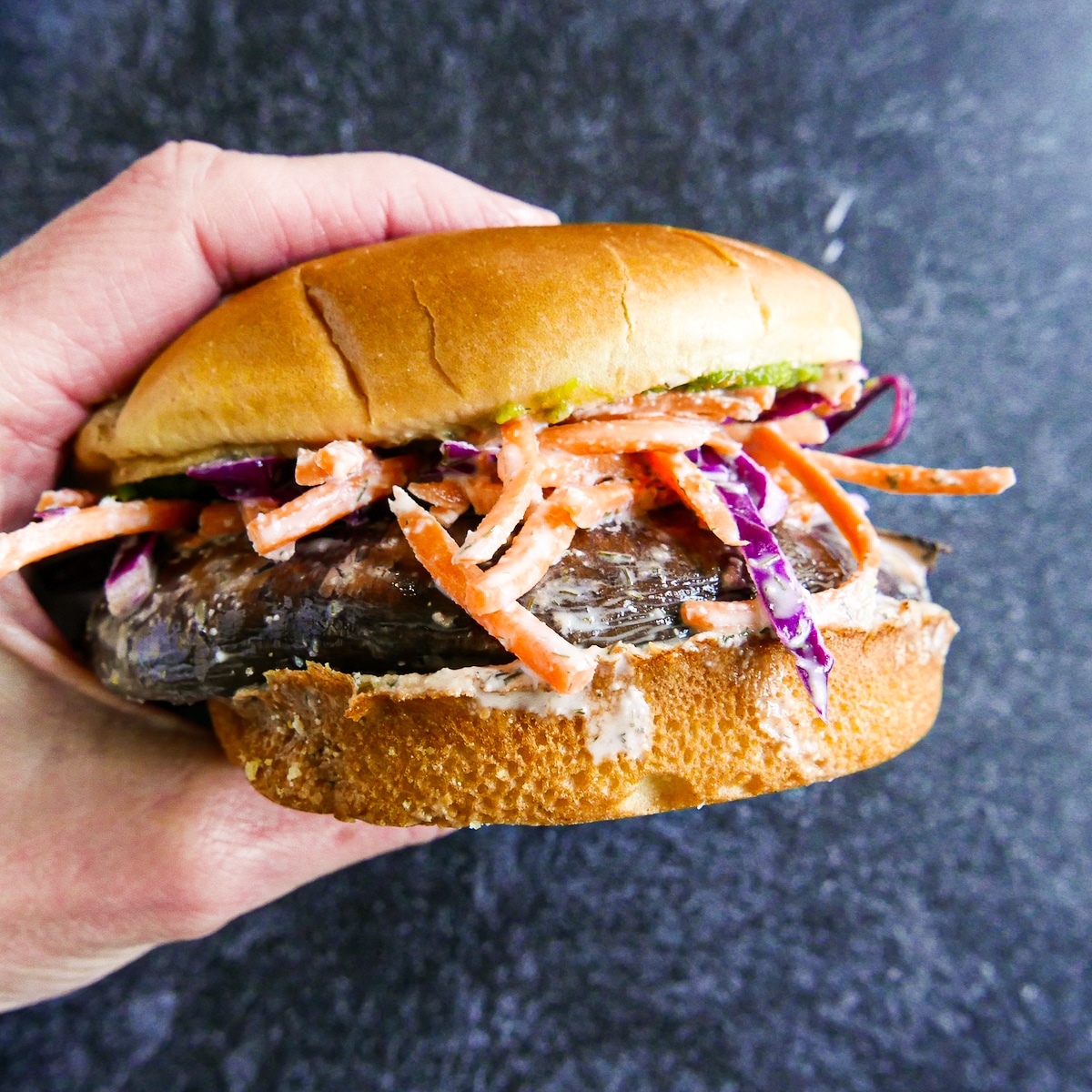 White hand holding up mushroom sandwich topped with slaw.