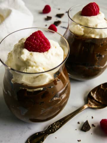 Two glass cups with avocado chocolate mousse and topped with whipped cream.