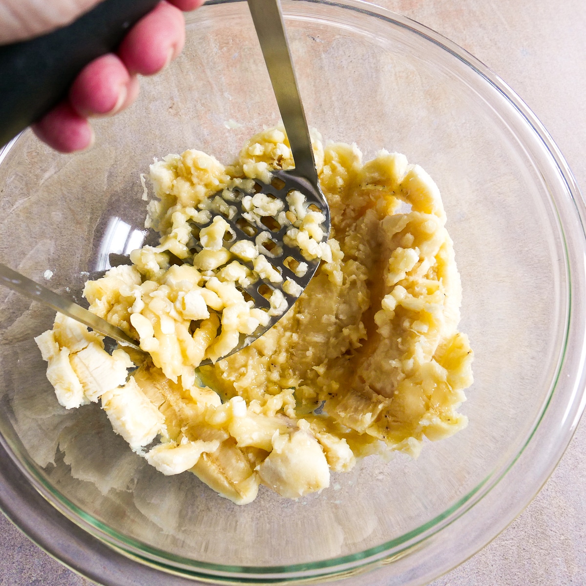 Bananas being mashed in a glass bowl.