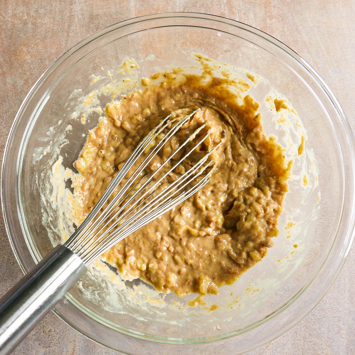 Mashed bananas and peanut butter being whisked in a glass bowl.