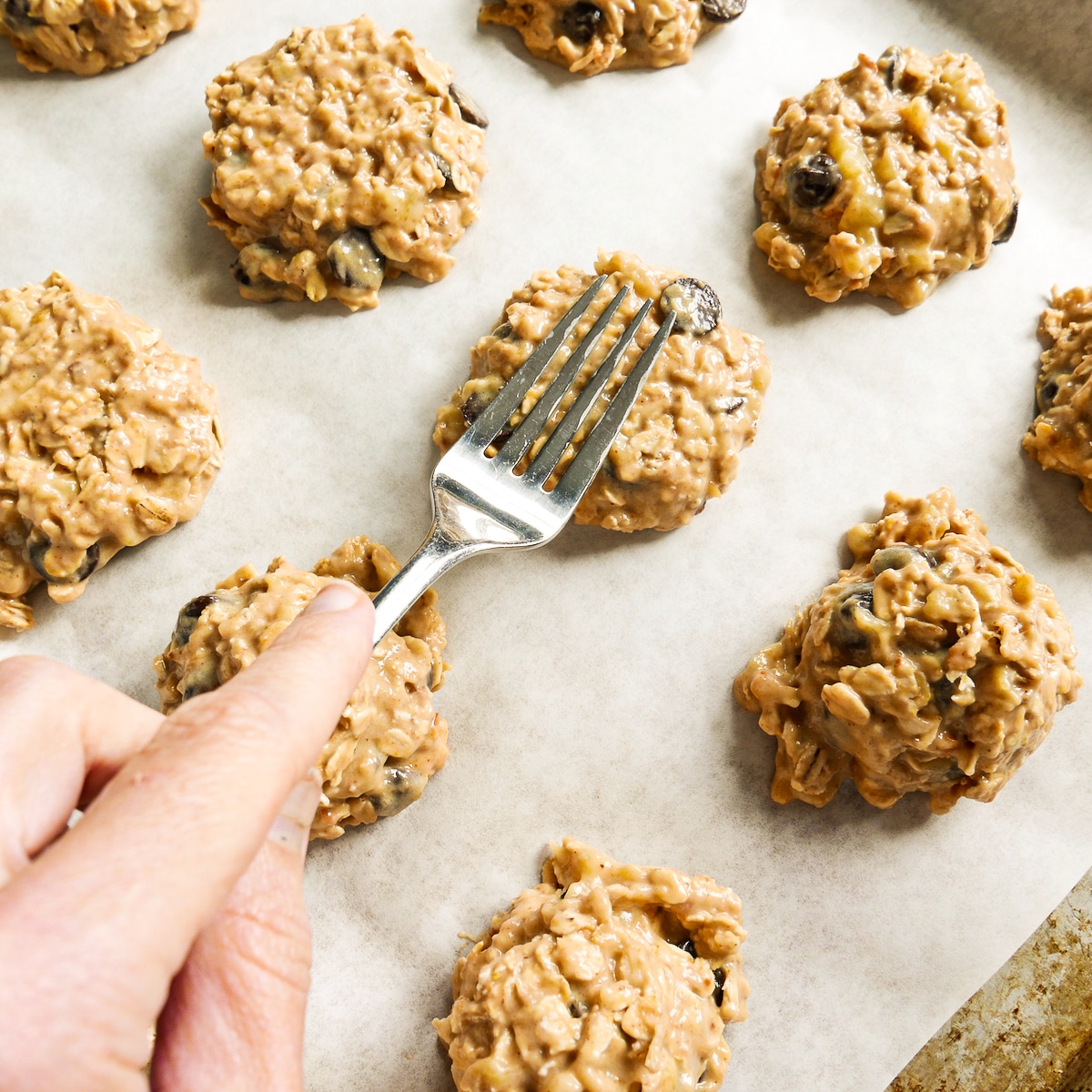 Fork pressing down on cookies arranged on a baking sheet.