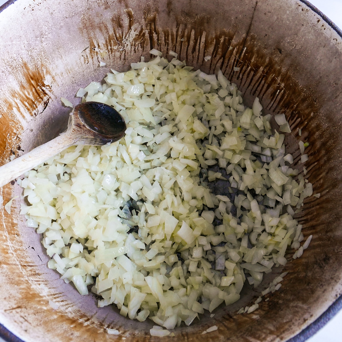 Onion cooking in a large Dutch oven with wooden spoon.