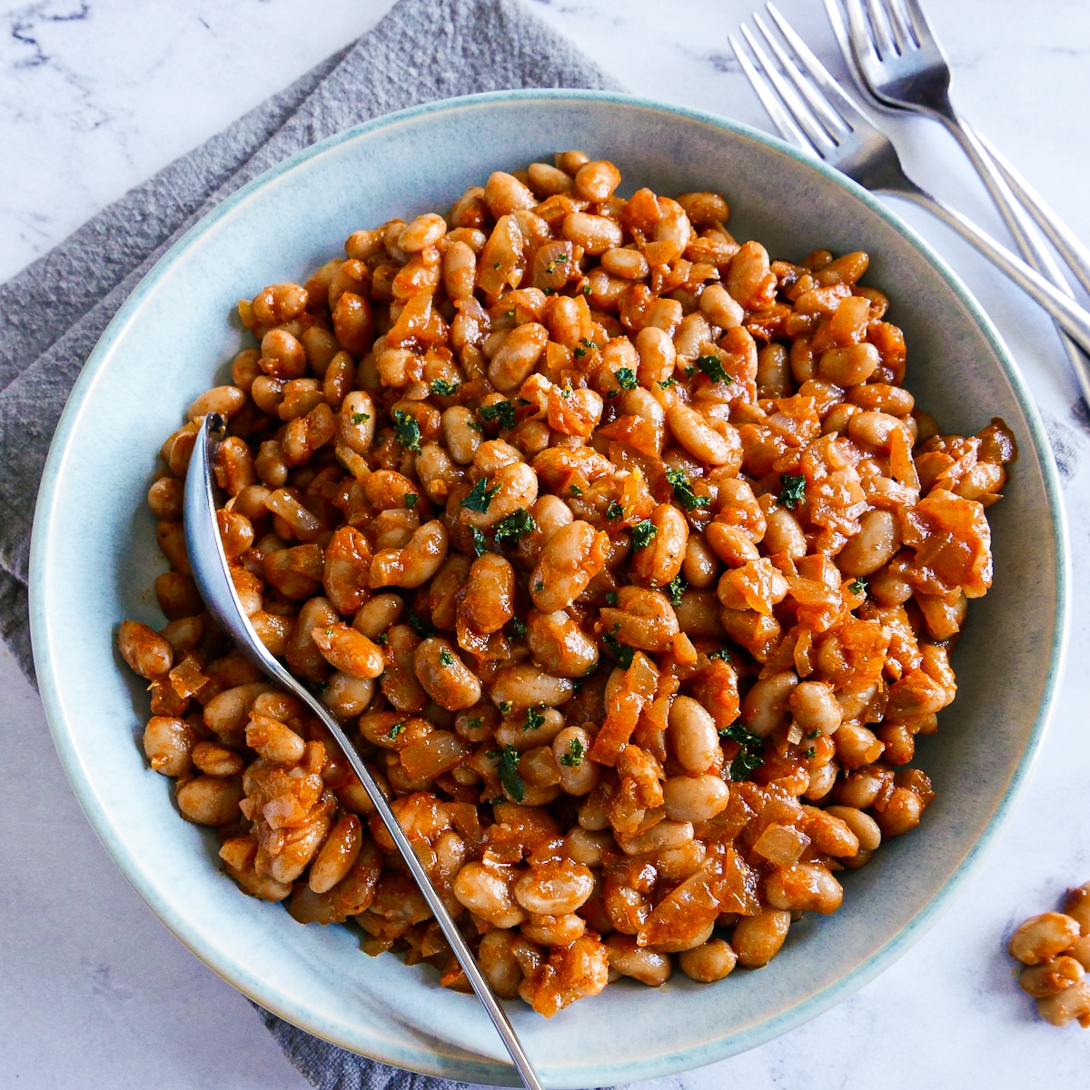 Bowl of baked beans with a spoon resting on a napkin.