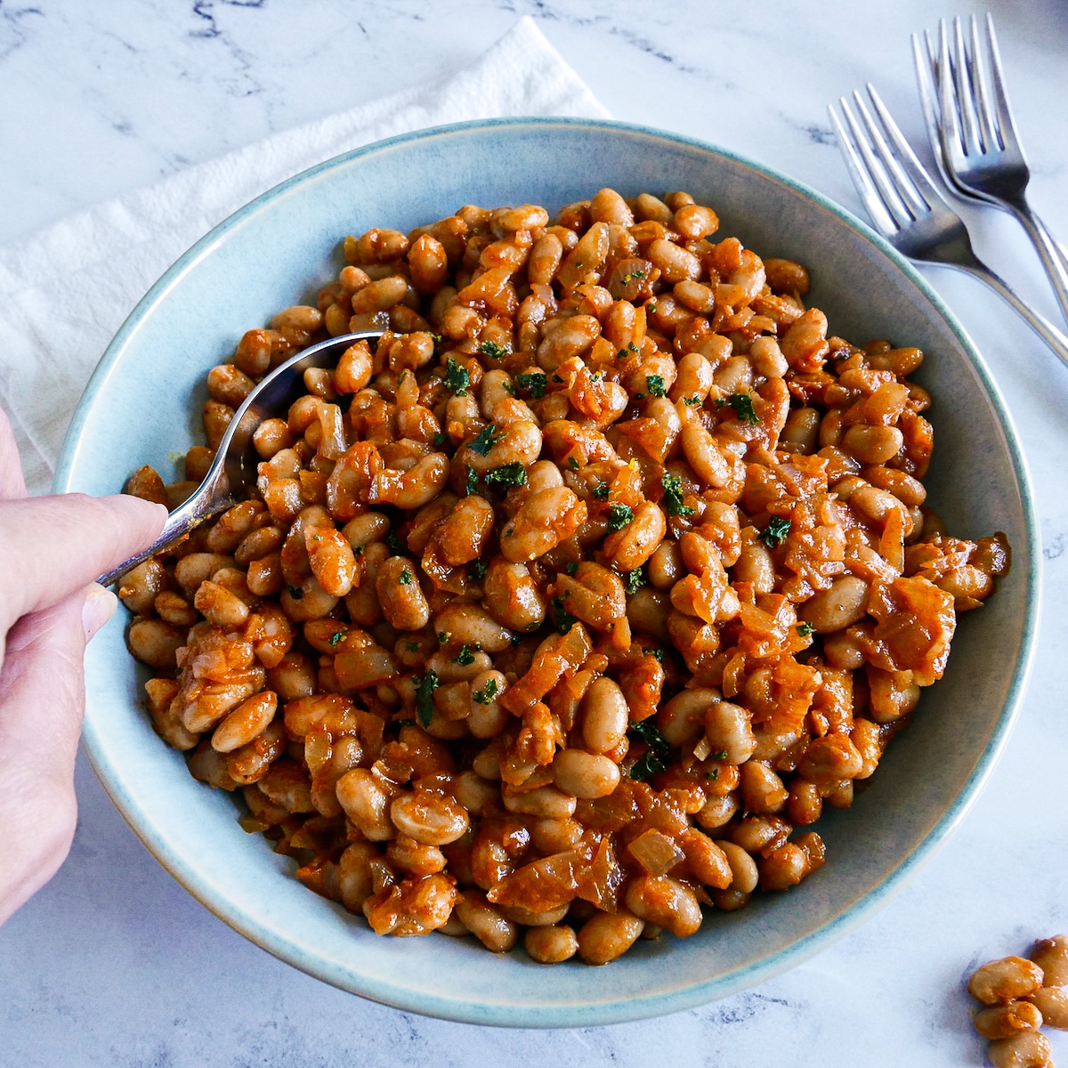 Hand scooping up beans with a spoon.