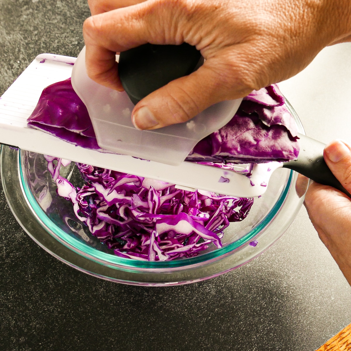 Hand demonstrating how to cut cabbage using a mandolin.