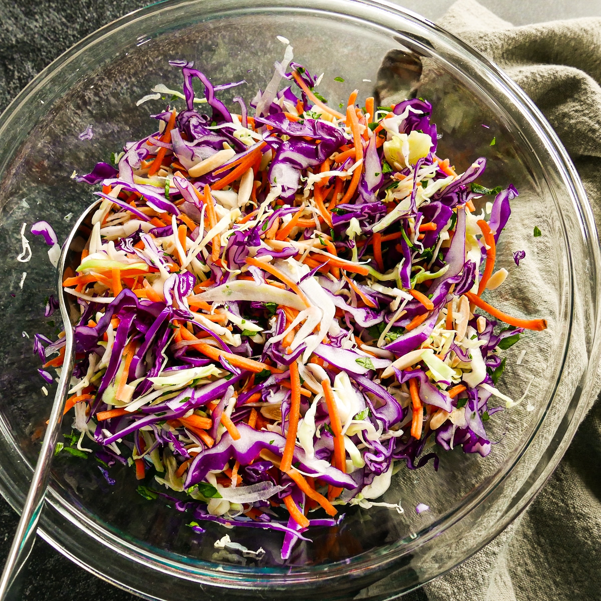 Cabbages, carrots, parsley, and almonds mixed together in a mixing bowl. 