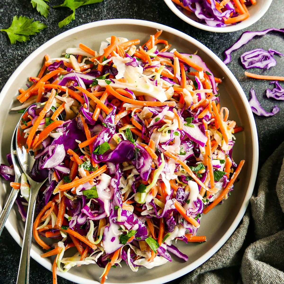 Assembled cabbage slaw on a gray plate with two serving spoons.