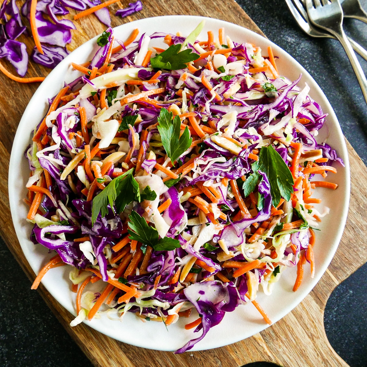 Purple cabbage slaw arranged on a white serving platter with two forks.