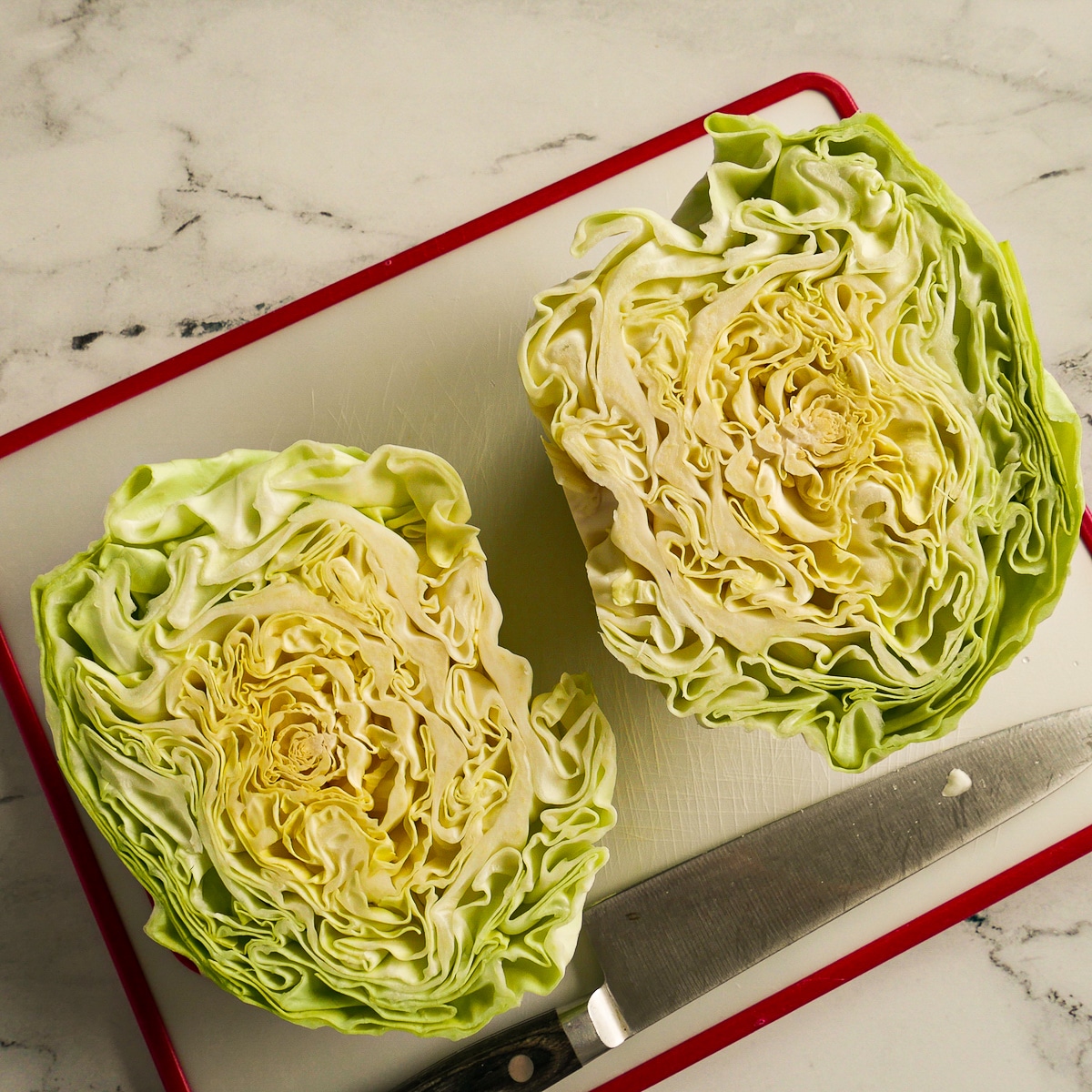 Two cabbage halves resting on a cutting board with a knife.