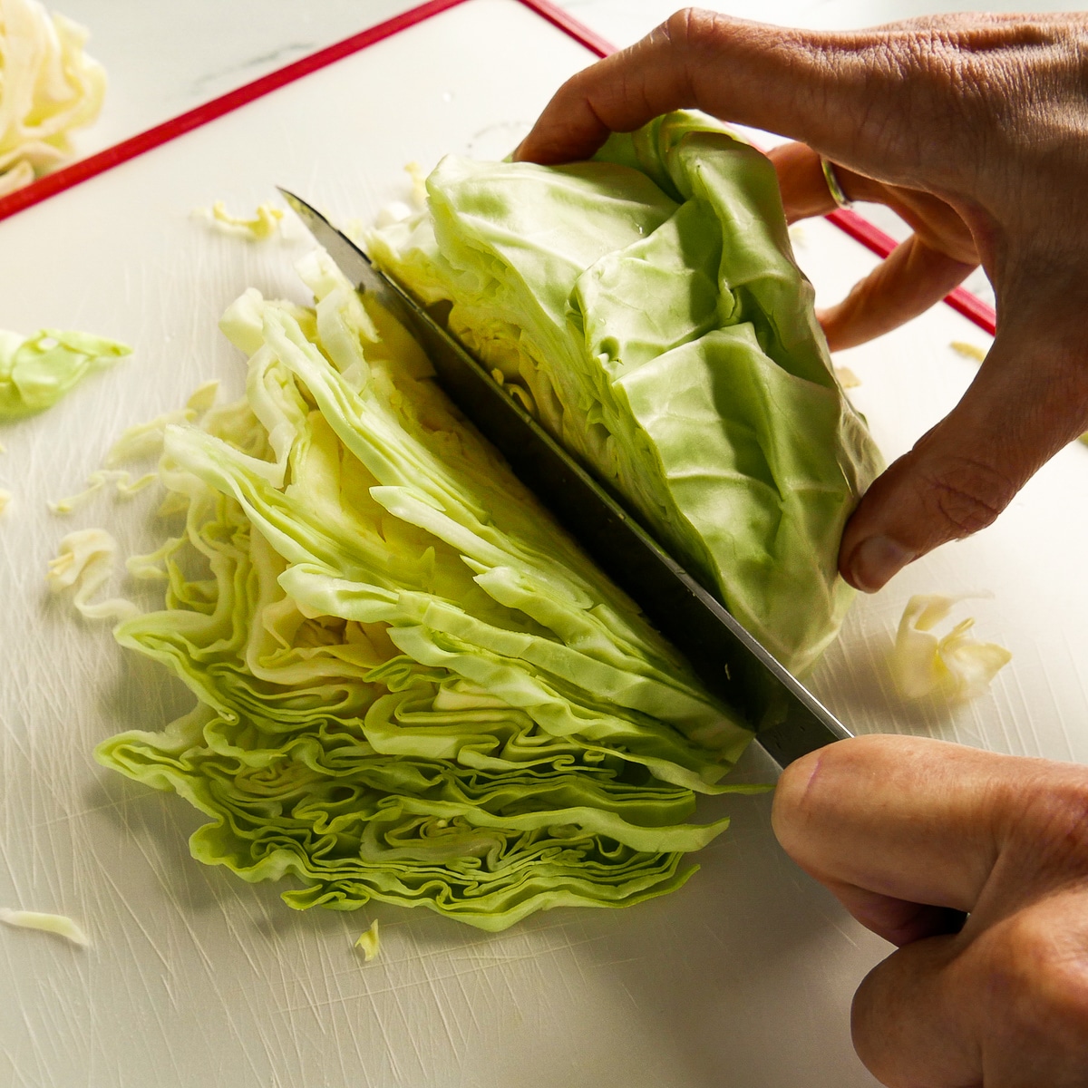 Cabbage being sliced by hand on a white cutting board.