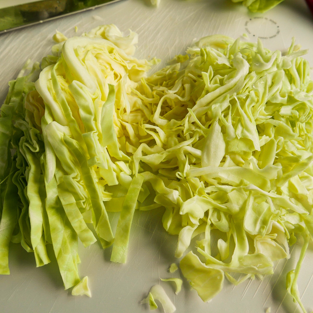 Two piles of sliced green cabbage resting on a cutting board.