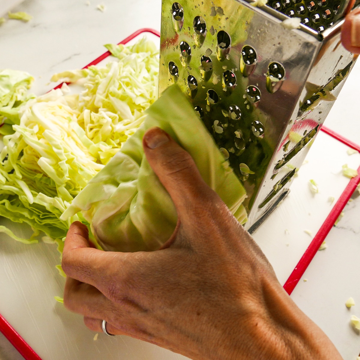 Hand shredding cabbage using a box grater.