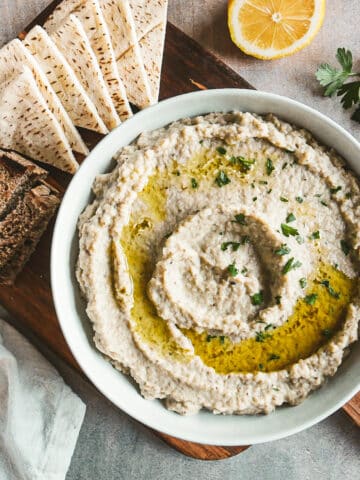 mutabal in a bowl resting on a cutting board with pita.