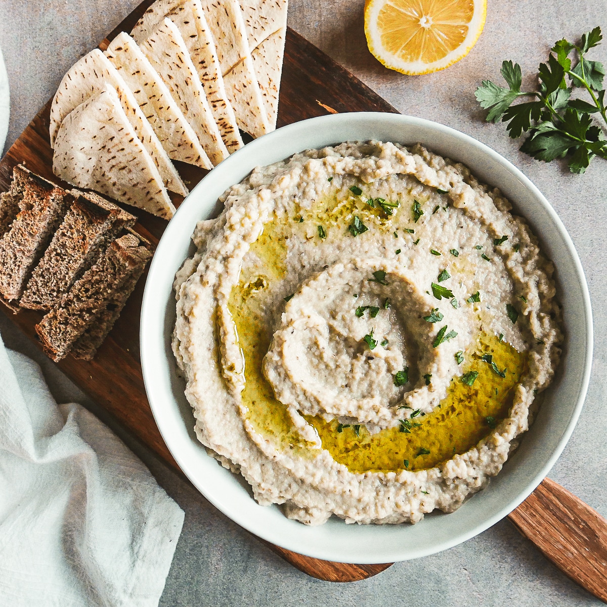 mutabal in a bowl resting on a cutting board with pita.