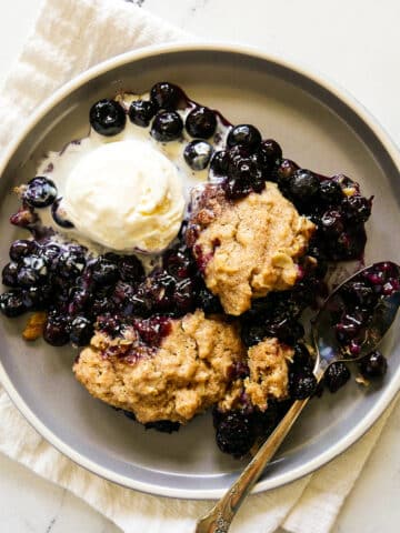 plate of blueberry cobbler with ice cream and a spoon resting on a white napkin.