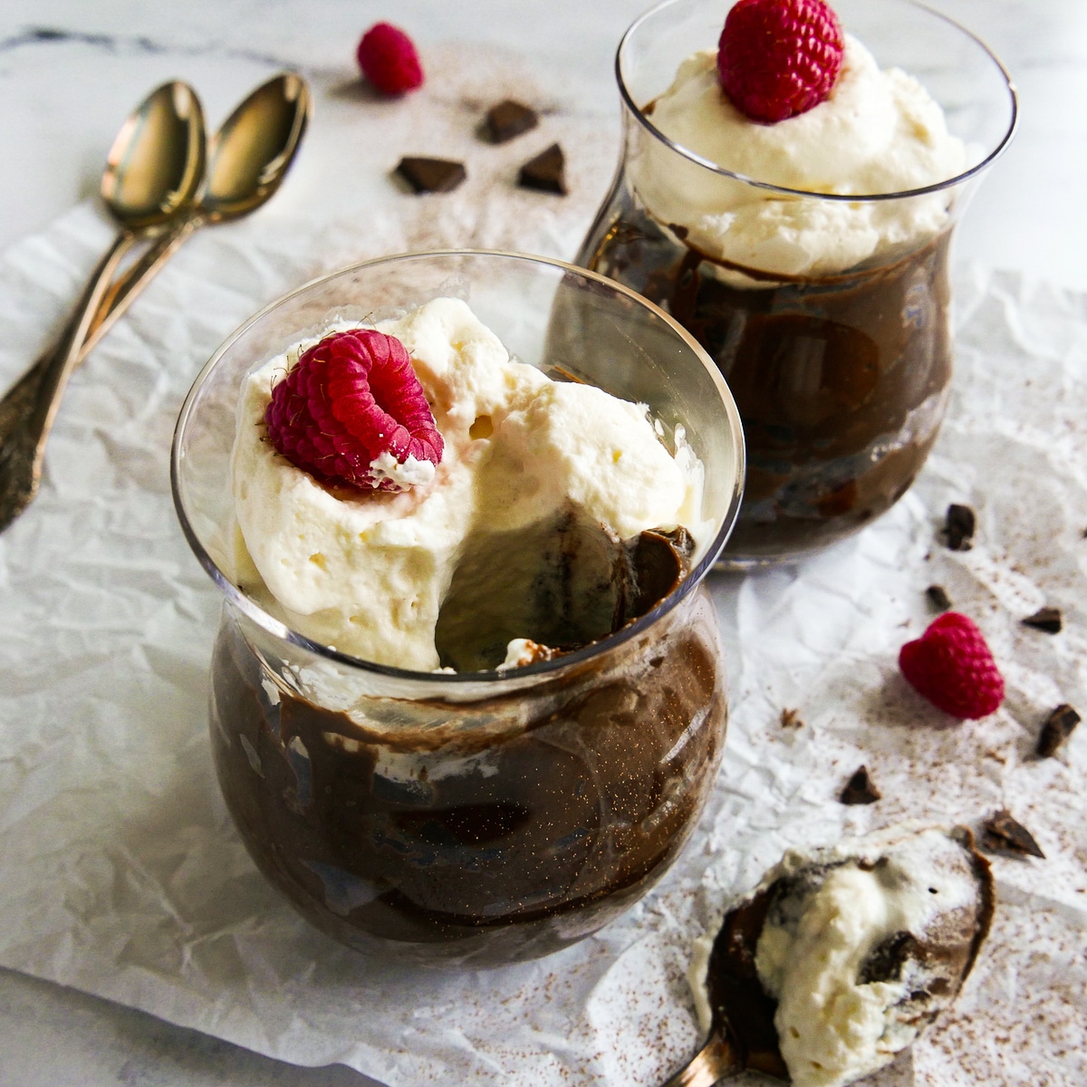Two cups of chocolate pudding with two spoons in the background.