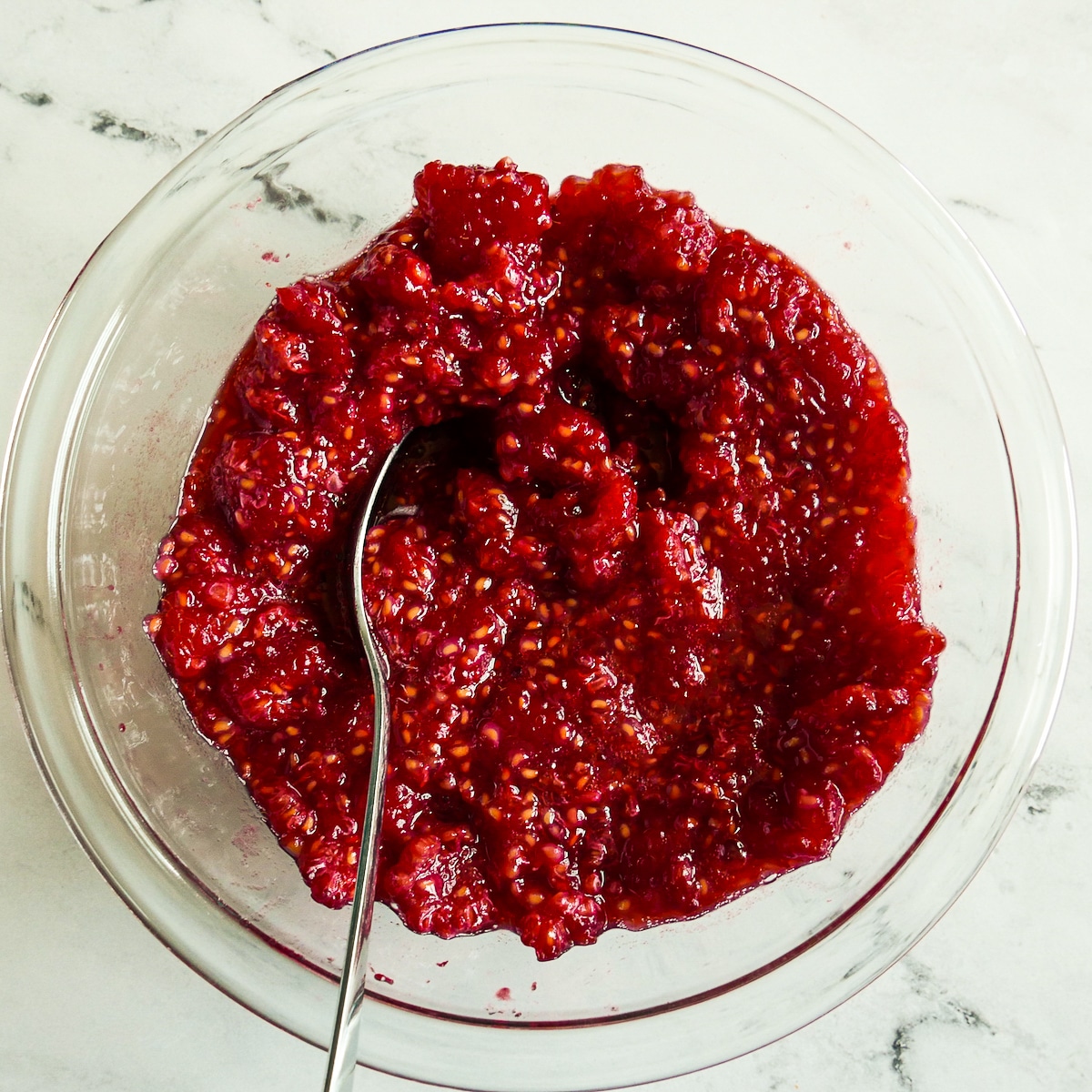 Raspberries mashed in a large bowl.