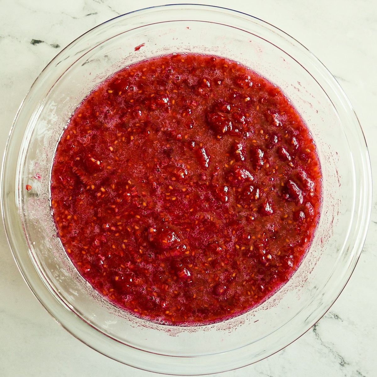Sugar mixed into mashed raspberries in a large bowl.