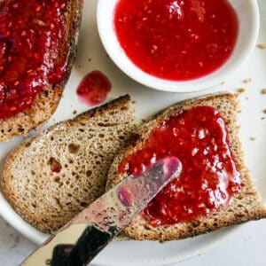 Knife spreading raspberry jam onto a piece of toast.