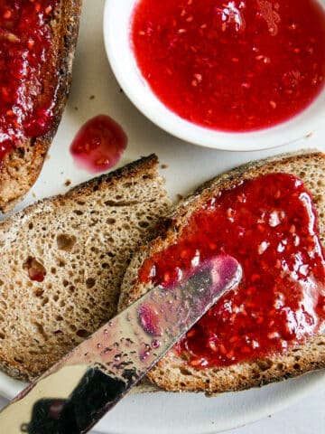 Knife spreading raspberry jam onto a piece of toast.