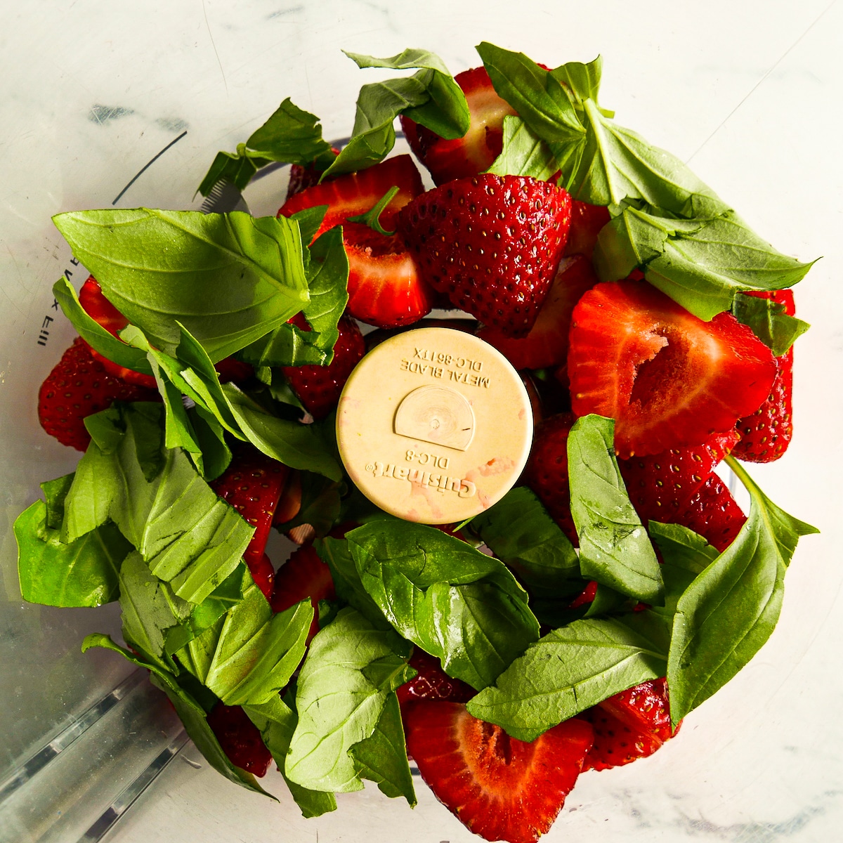 Sliced strawberries and chopped basil in a food processor.