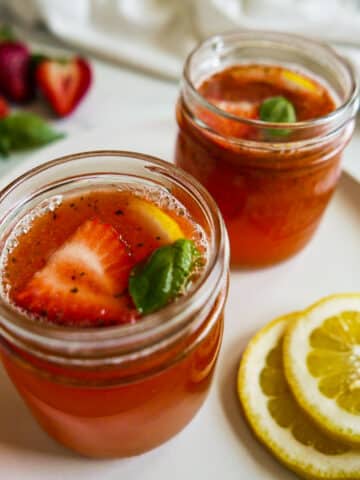 Two glass jars filled with strawberry basil lemonade and garnished with fresh basil.