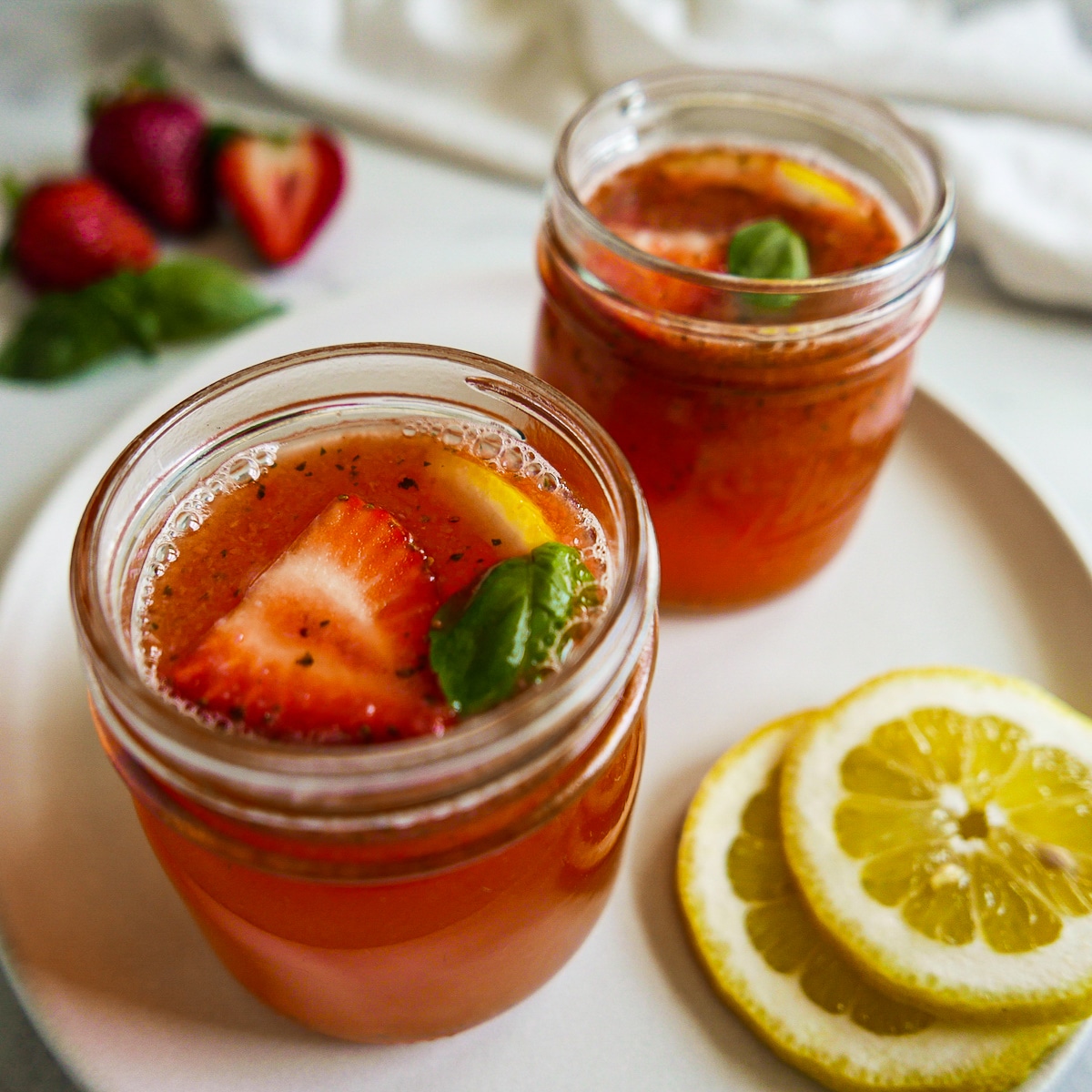 Two glass jars filled with strawberry basil lemonade and garnished with fresh basil.