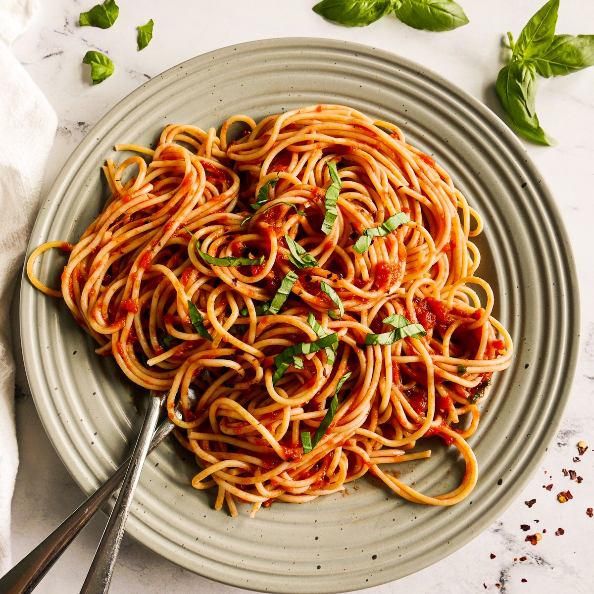 Spaghetti noodles tossed with tomato sauce and arranged on a plate.