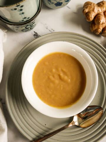 Homemade miso sauce in a small white cup resting on a gray plate.