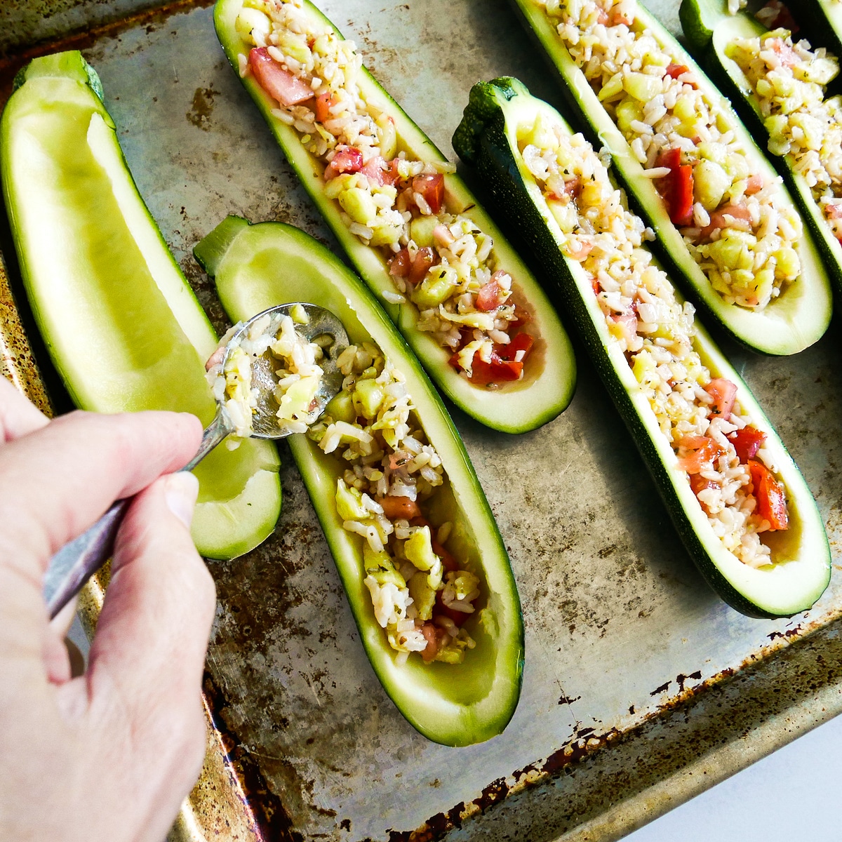 distributing-rice-mixture.jpg Using a spoon to distribute the rice mixture among the hollowed out zucchini.