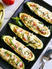 Five stuffed zucchini boats arranged on a platter with fresh basil.