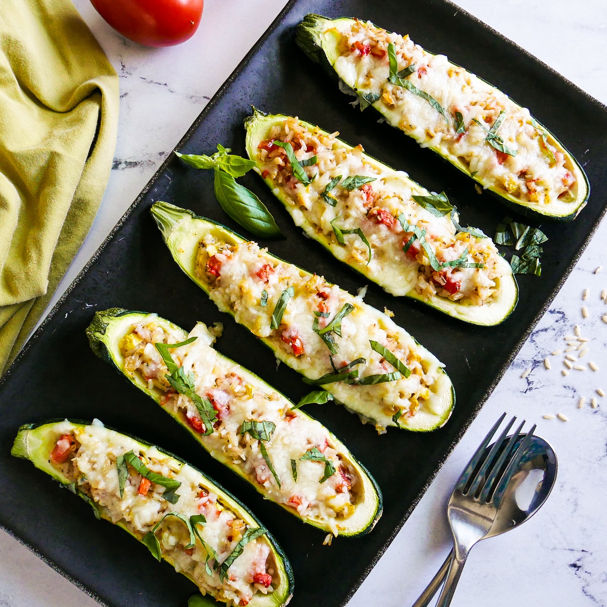 Five stuffed zucchini boats arranged on a platter with fresh basil.