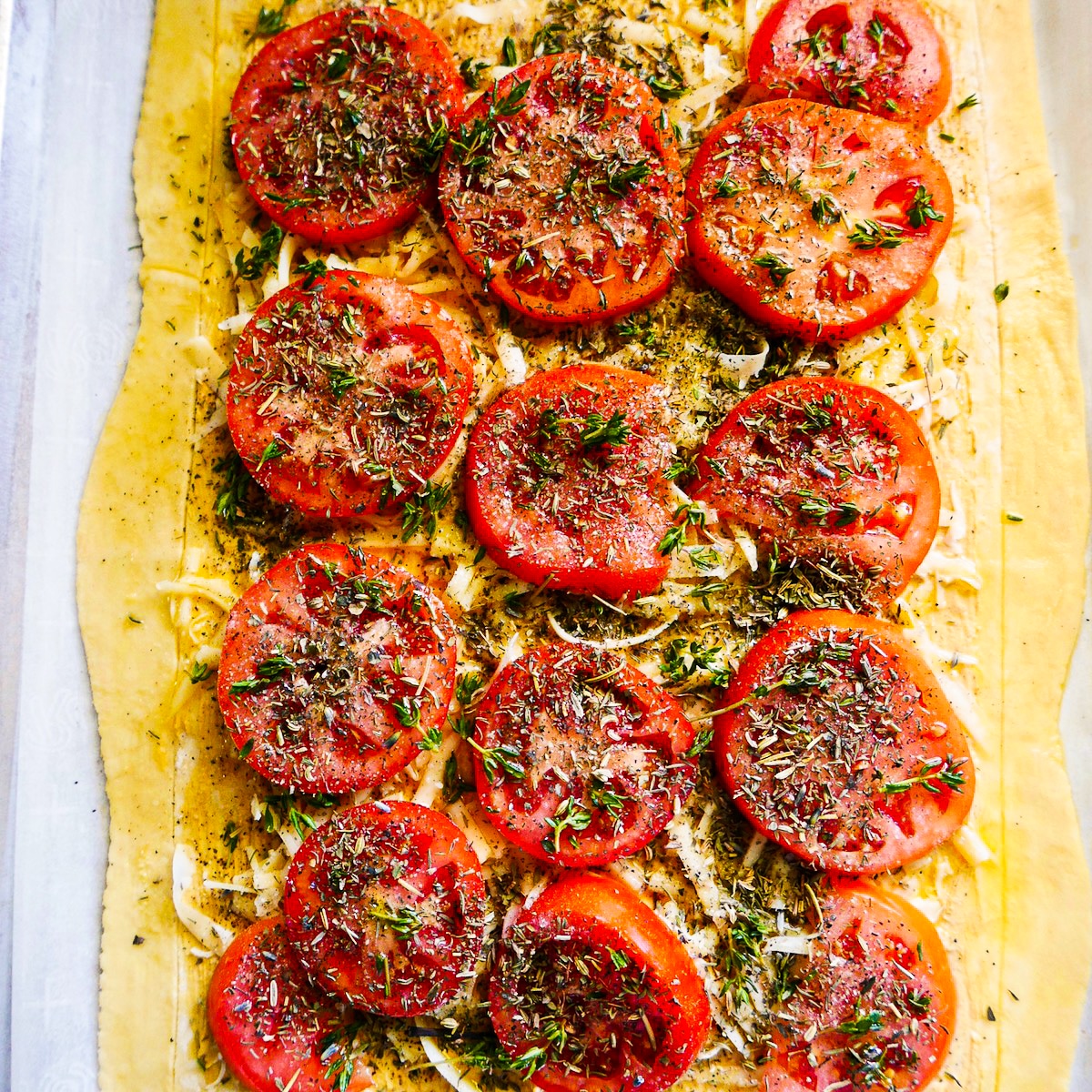 Sliced tomatoes, fresh thyme, and Herbes de Provence placed on pastry.